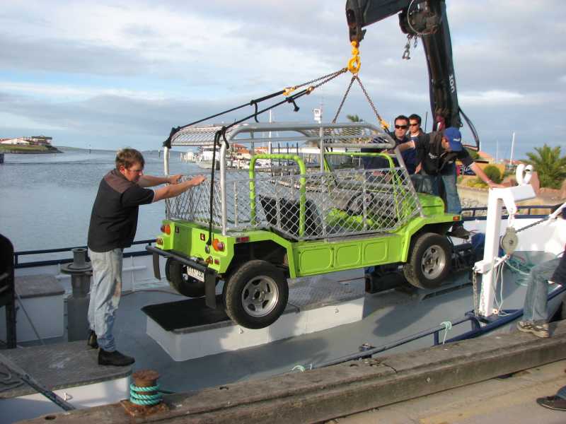 Image of green Moke fitted with shark cage being lifted onto the boat. 
